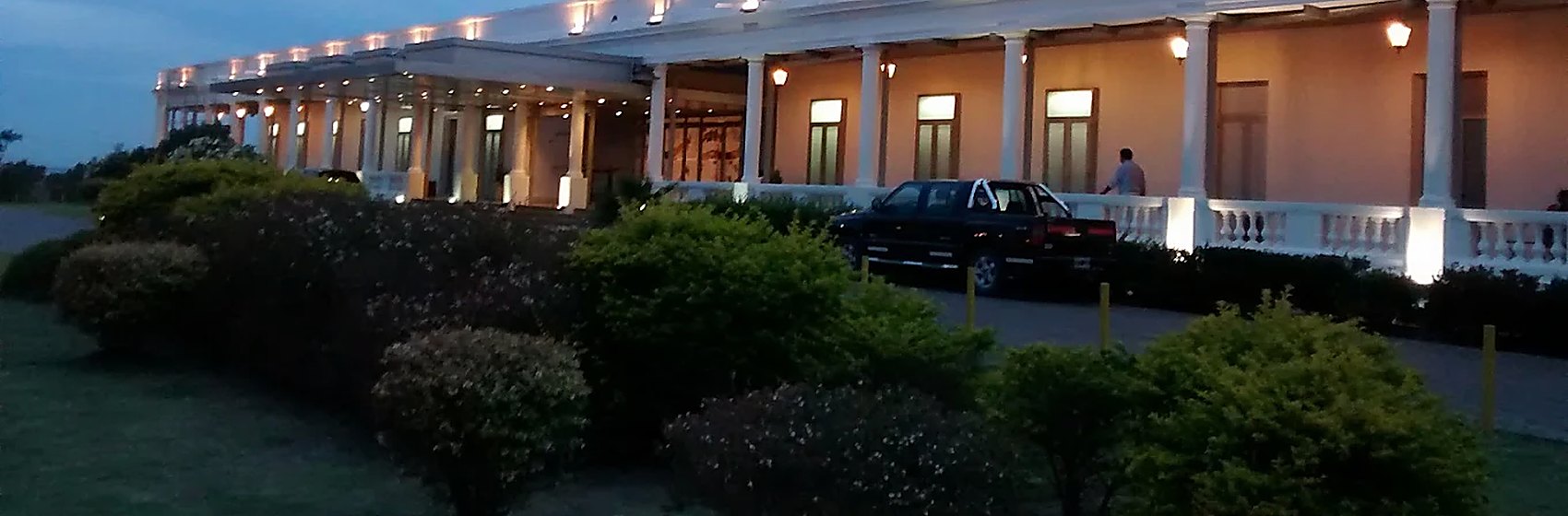 Galería de columnas iluminada al atardecer, con jardín y balaustrada en primer plano.