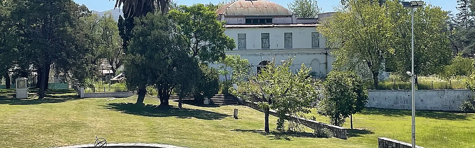 Parque con césped, palmeras y un edificio antiguo de cúpula al fondo.