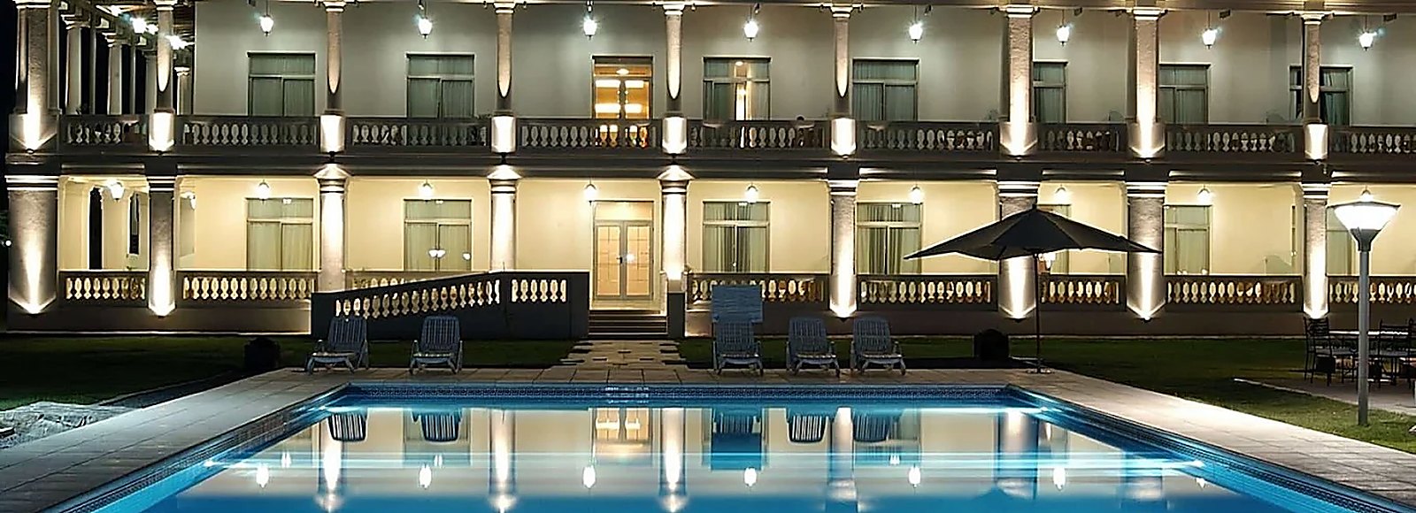 Casona iluminada de noche con galería de columnas reflejada en una pileta.