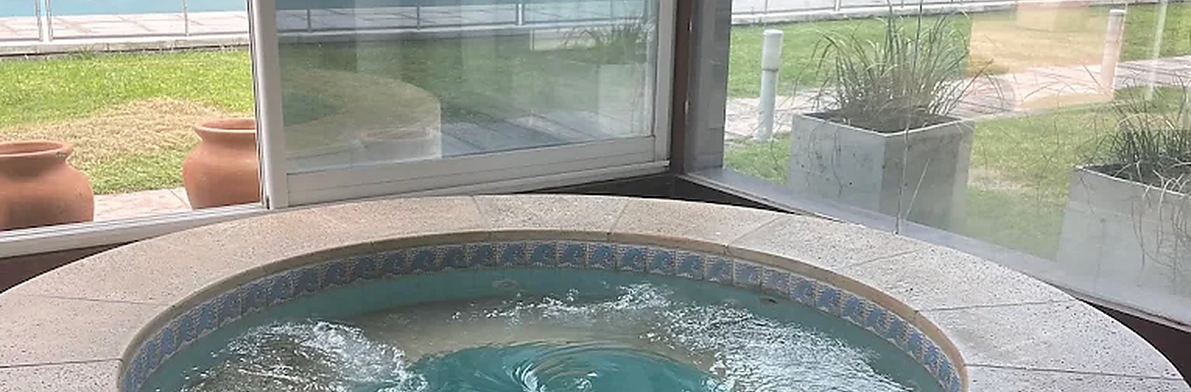 Hidromasaje circular bajo techo, con ventanal hacia el jardín y la pileta exterior.